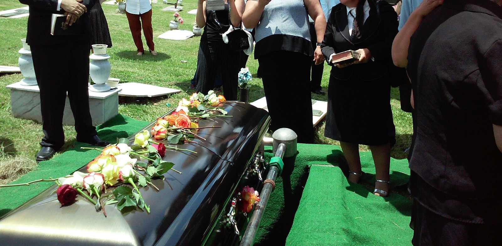 A group of people are standing around a coffin at a funeral.